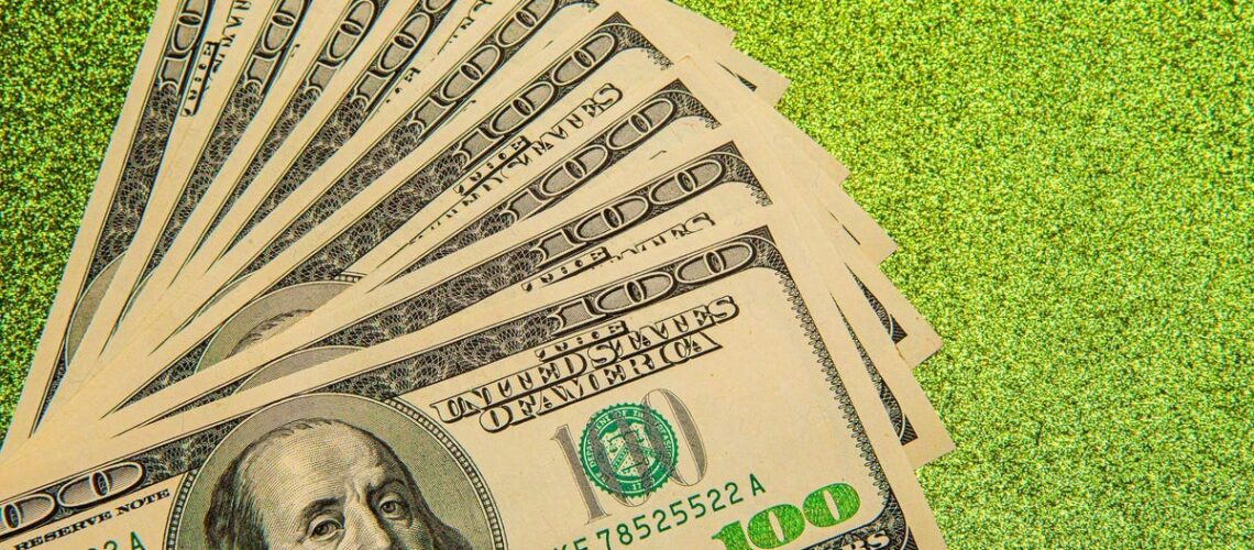 A stack of hundred dollar bills are laid out on a green background.