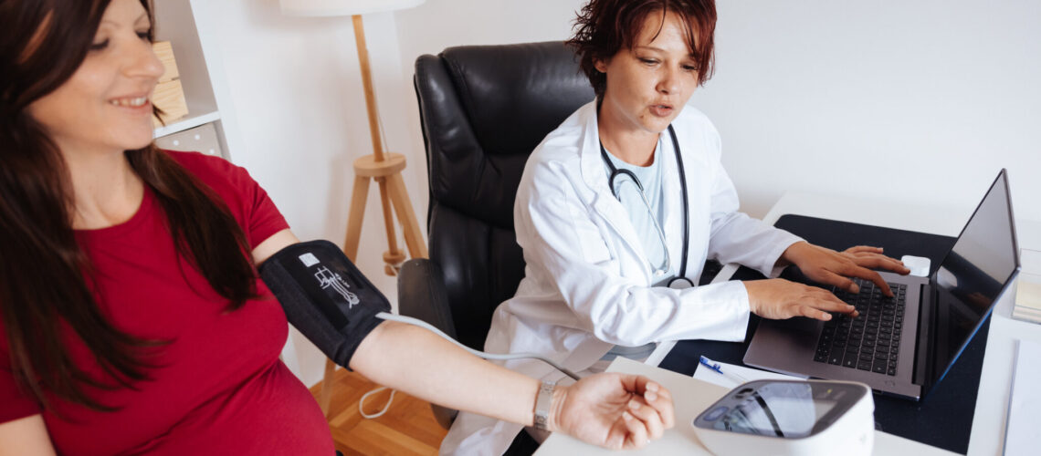 doctor takes the blood pressure of pregnant woman at doctor's office